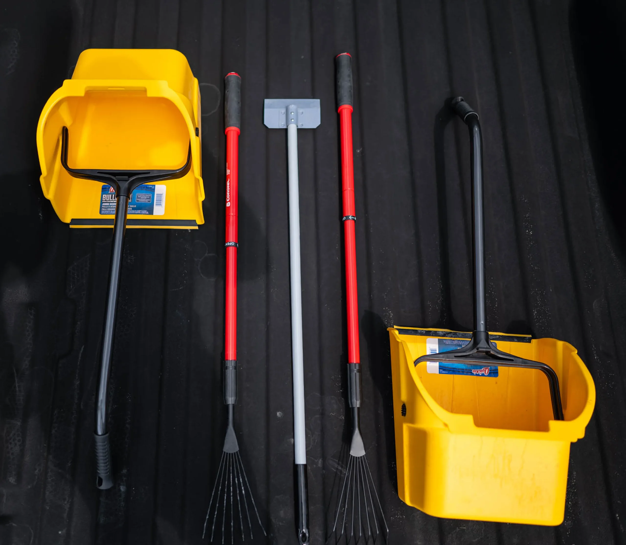 image 2 Two yellow snow shovels and two red-handled snow rakes on a black surface.