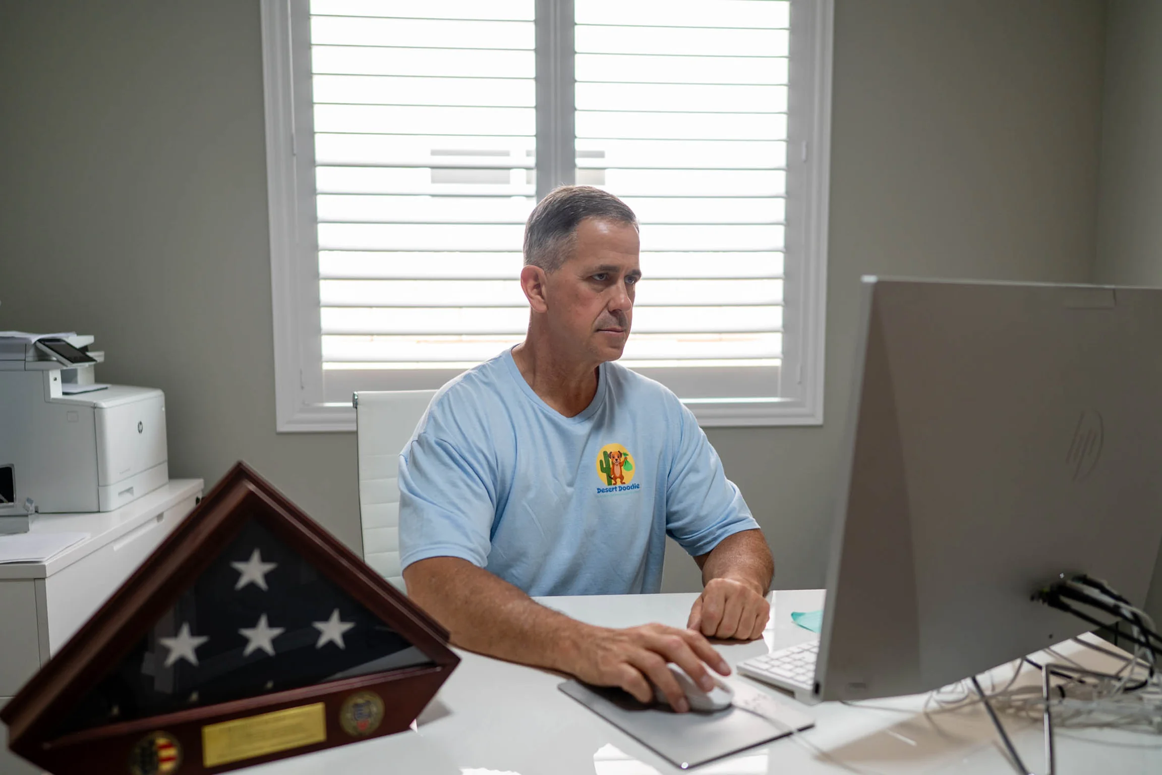 Man in light blue shirt working on a laptop at a desk.